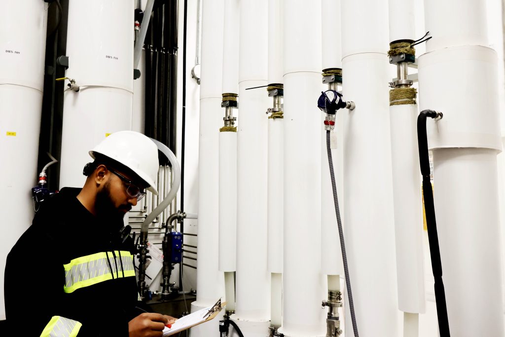 An Isowater employee standing in front of white pipes looking at a clipboard.